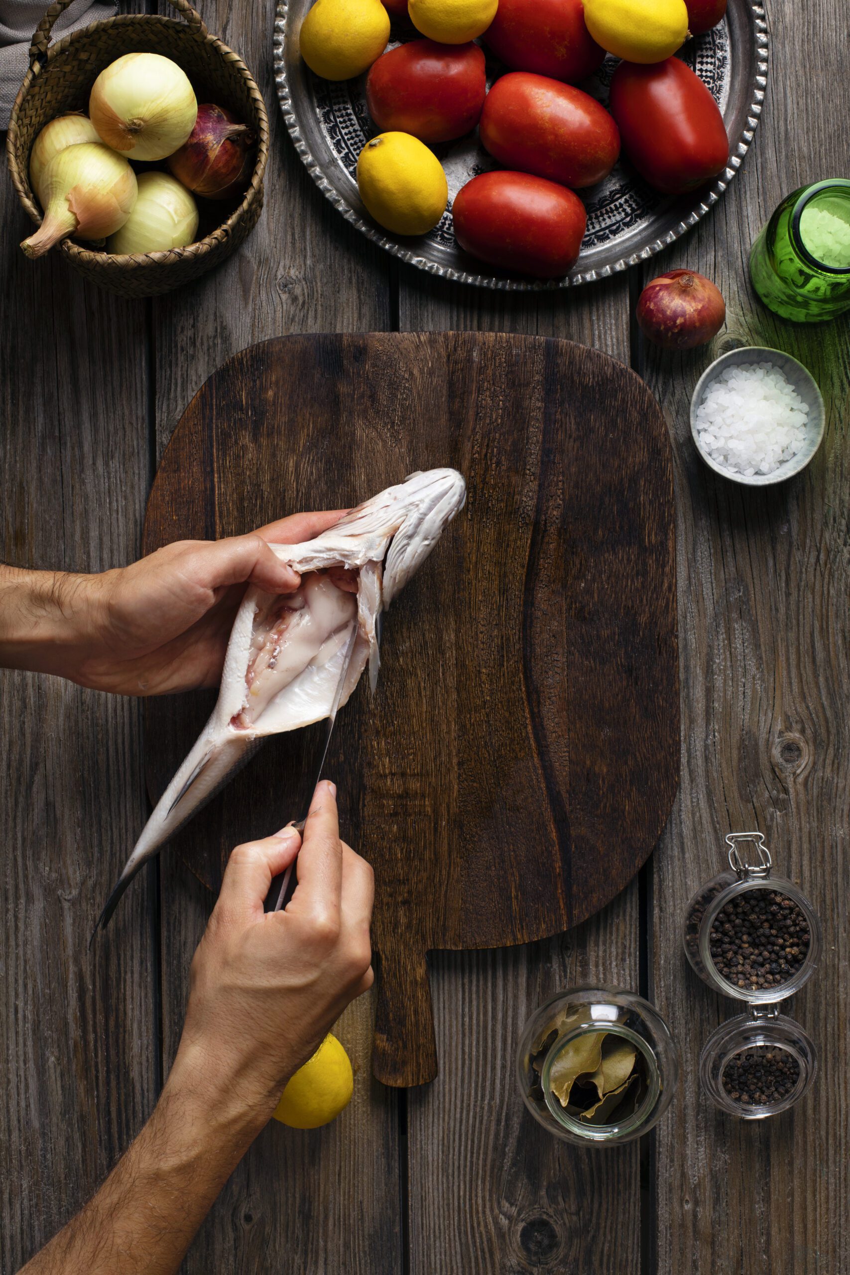 image of a person cleaning a fish on a wooden cutting board with veggies around the board. 